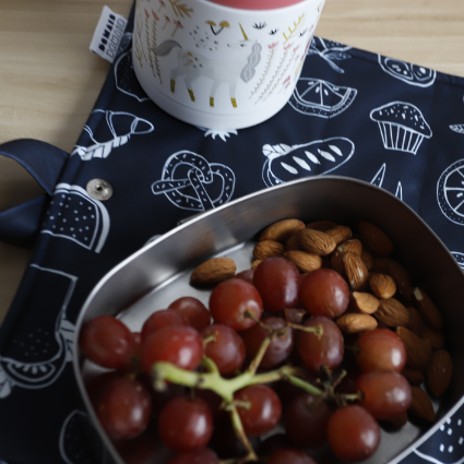 Plant en acier inyxidable contenant des raisins et des amandes déposé sur un napperons à motifs noir et accompagné d'un contenant isolant.