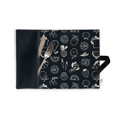 Napperon portatif noir Eco Loco avec des motifs de fruits et de légumes blancs montrant des ustensils dans la pochette et une ganse pour le rouler sur un fond blanc. 