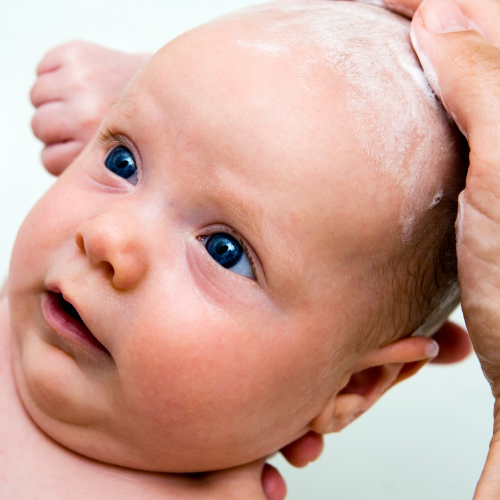 Un bébé se fait laver les cheveux avec une barre de shampoing adapté à lui. 