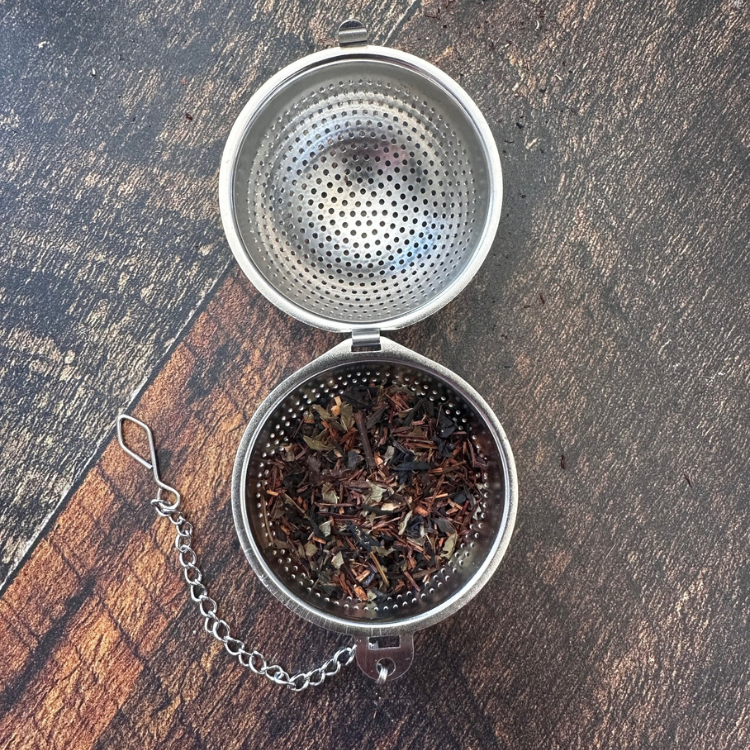 Infuseur pour thé en acier inoxydable contenant de la tisane sur une planche de bois