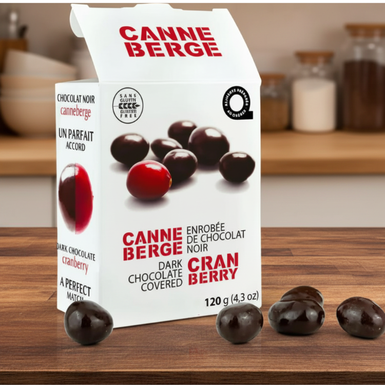 Boite de canneberges enrobée de chocolat noir ouverte avec quelques canneberge au chocolat sortie de la boite déposé sur un comptoir en bois dans une cuisine.   