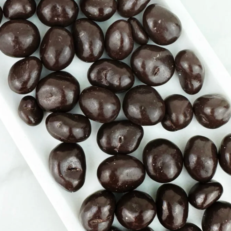 Des boules brunes représentant des canneberges enrobées de chocolat noir dans un plat en céramique blanc. 