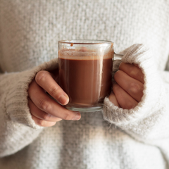 Tasse de chocolat chaud tenue dans deux mains par une dame dans un chandail de laine. 