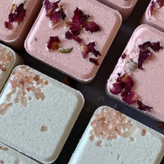 Des petits carrés roses et vert pâles recouverts de sels et de fleurs représentant des bombes de bain. 