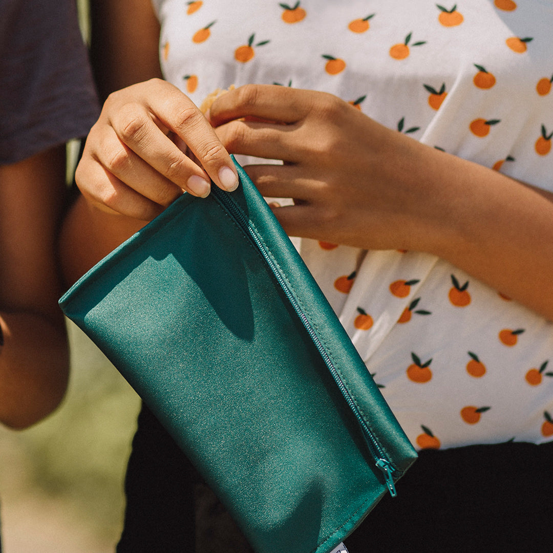 Gros plan sur les mains d'une jeune femme avec un chandail à motif d'oranges qui tient un sac à collation en tissu vert uni dans ses mains