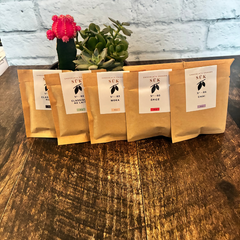 Les 5 saveurs de chocolat chauds en sachet kraft de la compagnie SÜK adossé à une plante sur une planche de bois. 