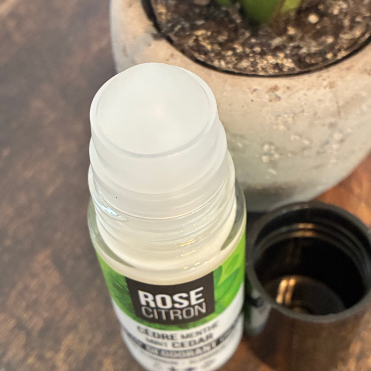 Bouteille de déodorant de la marque Rose  Citron ouverte pour voir la bille avec une étiquette verte sur un planche de pois, près d'une plante. 