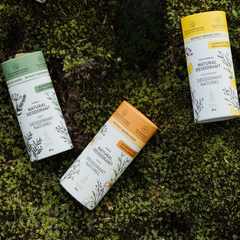 Trois tubes de déodorant de couleur verte, jaune et orange sur un lit de lichen vert avec des écritures en français et en anglais:  Deodorant naturel, sans bicarbonate, Tanit et des dessins de végétaux. 