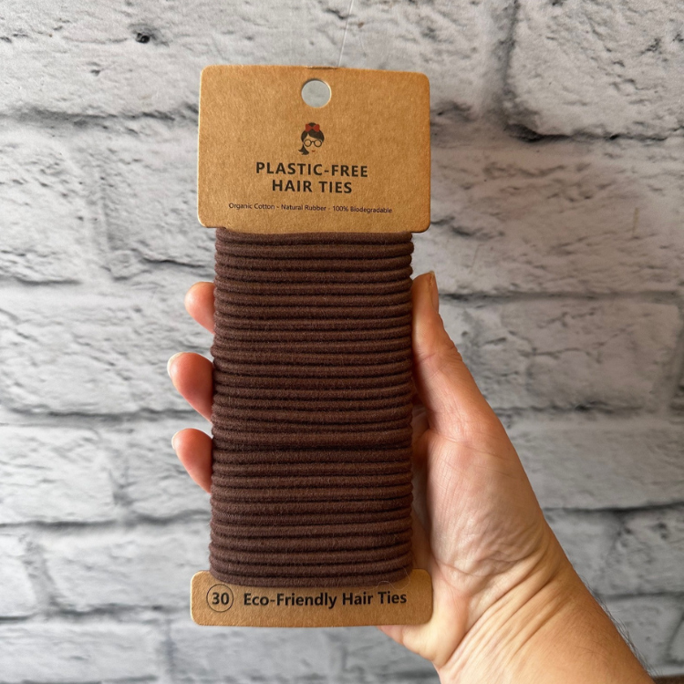Paquet de 30 élastiques à cheveux sans plastique en silicone naturel  de couleur brun tenu dans une main avec un fond de brique