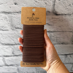 Paquet de 30 élastiques à cheveux sans plastique en silicone naturel  de couleur brun tenu dans une main avec un fond de brique