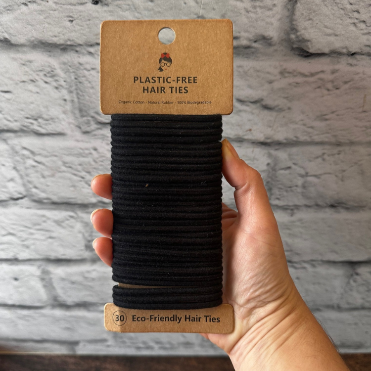 Paquet de 30 élastiques à cheveux sans plastique en silicone naturel  de couleur noir tenu dans une main avec un fond de brique