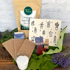 Ensemble de produits écoresponsable Nettoyant à cuvette avec un chiffon suédois, des éponges à récurer brunes, un cake vaisselle, un shampoing solide en forme de coeur, de la soie dentaire compostable sur un fond de feuilles vertes, de lavandes et un mur de briques blanches