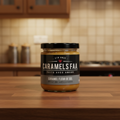 Une pot avec une étiquette sur la quel est inscrit Caramels FAA faits avec avoir caramel fleur de sel avec un couvercle noir déposé sur un comptoir de cuisine en bois avec un arrière plan de cuisine. 