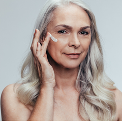 Belle femme à la chevelure blanche et longue et aux yeux brun appliquant de la crème blanche sur son visage. 