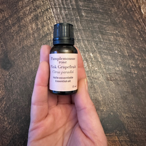 Flacon d'huile essentielle de pamplemousse rose tenu dans une main au-dessus d'une planche de bois