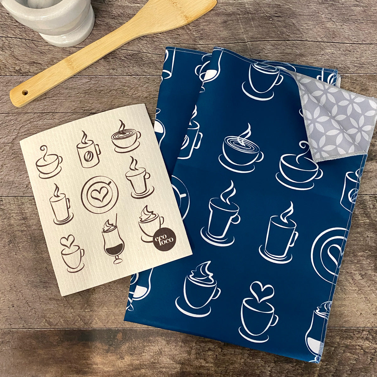 Un linge à vaisselle en microfibre à motifs de tasses sur fond bleu et un chiffon suédois beige à motifs de tasse à café sur un comptoir de bois foncé