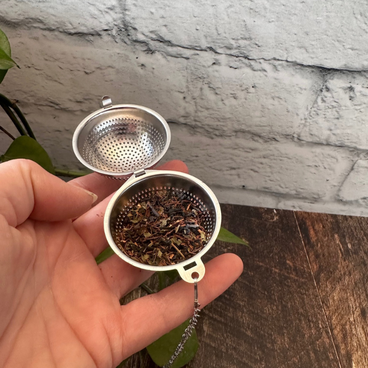 Infuseur pour thé en acier inoxydable avec une chaîne dans une main avec un fond de brique, de bois et de plante