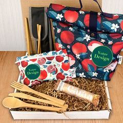 Une boîte cadeau écoresponsable avec à l'intérieur une boite à lunch, un sac à collation réutilisable, une barre de chocolat caramel caraa et des ustensiles en bois
