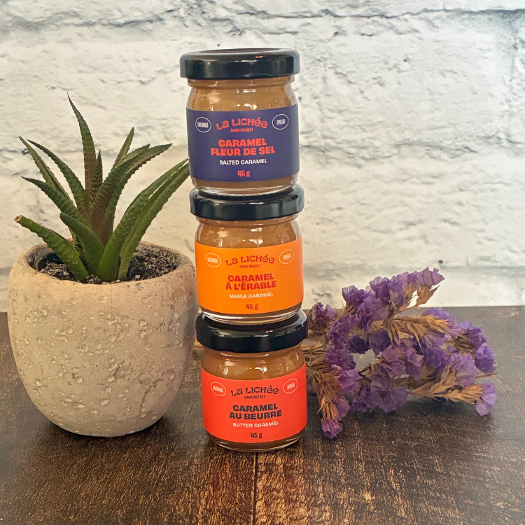 Trois petits pots de caramels un par dessus l'autre de l'entreprise québécoise La lichée (caramel salé, caramel à l'érable et caramel au beurre) à côté d'une plante et de fleurs. 