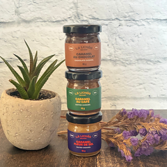 Trois petits pots de caramels un par dessus l'autre de l'entreprise québécoise La lichée (caramel salé, caramel au chocolat et caramel au café) à côté d'une plante et de fleurs. 