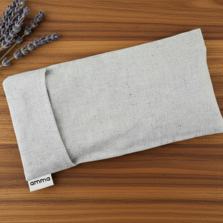 Pochette représentant un masque de relaxation rectangulaire de couleur sable de la marque Amma sur une planche en bois sur laquelle il est aussi déposé quelques branches de lavande séchée. 