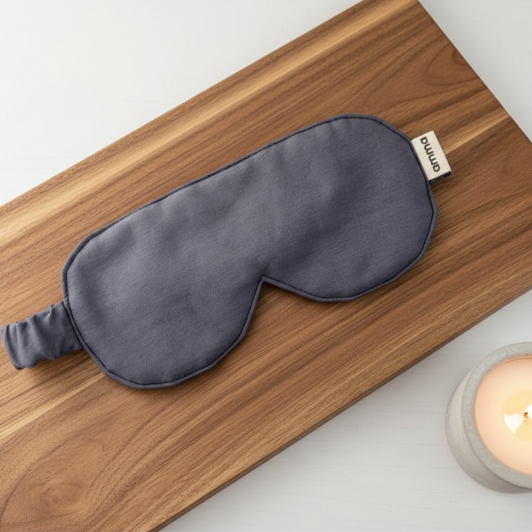 Un masque de nuit gris foncé de l marque Amma sur une planche de bois accompagné d'une chandelle dans un pot de ciment. 