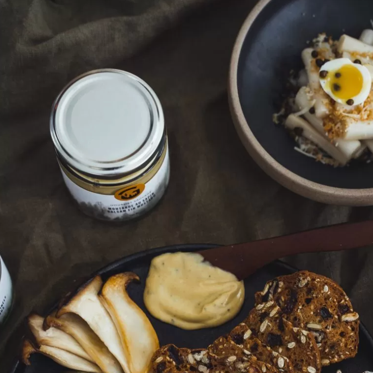 Pot de moutarde au champignons sauvages du Québec de la marque Gourmet sauvage, déposé sur un tissu noir et accompagné d'une salade et de craquelins. 