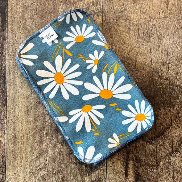 Papier de toilette lavable gris avec des motifs de marguerite déposé sur une planche de bois