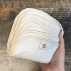 Une main qui tient du papier de toilette rectangulaire lavable beige en coton biologique avec une étiquette Eco Loco sur un fond de couleur bois foncé