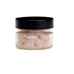 Pot de pastille propolis et miel pour les maux de gorge dans un contenant en verre et un couvercle noir sur fond blanc