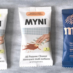 Petit sachet blanc écrit Myni Pamplemouse & mangue nettoyant multi surfaces sur un fond de textile gris