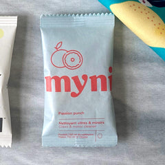 Petit sachet bleu pâle écrit Myni Passion punch nettoyant vitres & miroirs sur un fond de textile gris
