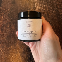 Bougie eucalyptus tenue dans une main sur un planche de bois