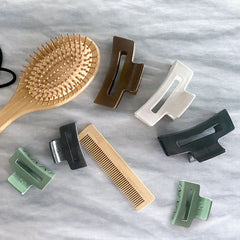 Pinces recyclées noires, vertes, blanches, brunes de l'entreprise Unique plastique sur fond blanc avec un brosse à cheveux en bois et un peigne de bois deux élastiques noirs