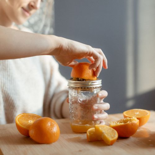 main qui presse une orange sur un pressoir en métal qui va sur un pot masson