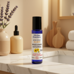 Bouteille bleu au capuchon noir de la marque Divine essence pour le soins des bleus et des bosses certifié biologique par Eco Cert déposé sur un comptoir de salle de bain avec des serviette et un pot de fleur séchéesé