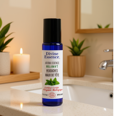 Bouteille bleu au capuchon noir de la marque Divine essence pour le soins Maux de tête certifié biologique par Eco Cert déposé sur un comptoir de salle de bain avec une chandelle et un plante en arrière plan. 