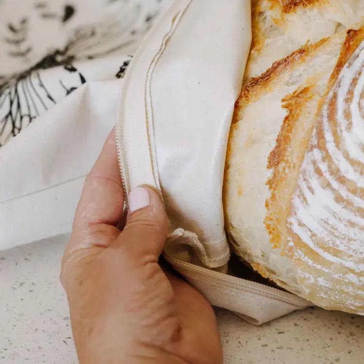 Une miche à pain dans un sac de couleur naturel réutilisable tenu pas une main de femme. 