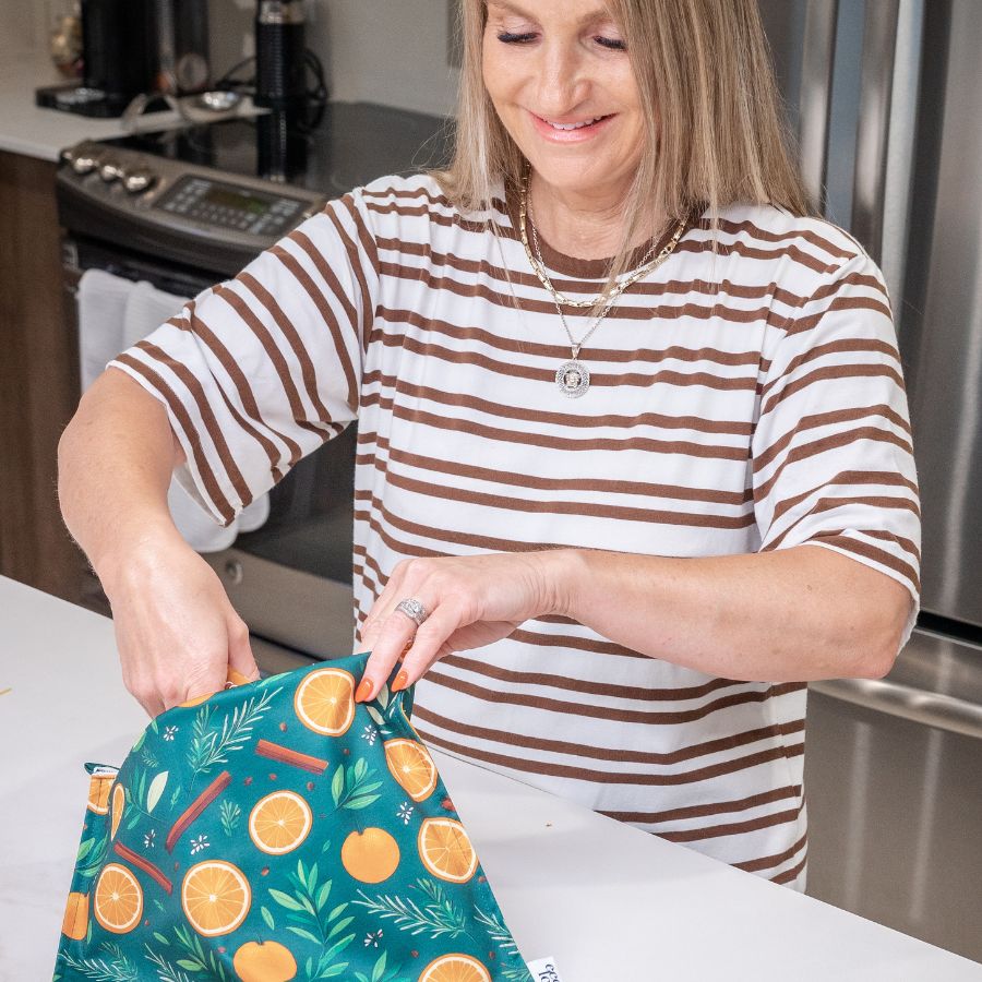 Femme souriante aux cheveux blonds qui tien un sac réutilisable à congélation dans un décor de cuisine