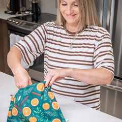 Femme souriante aux cheveux blonds qui tien un sac réutilisable à congélation dans un décor de cuisine