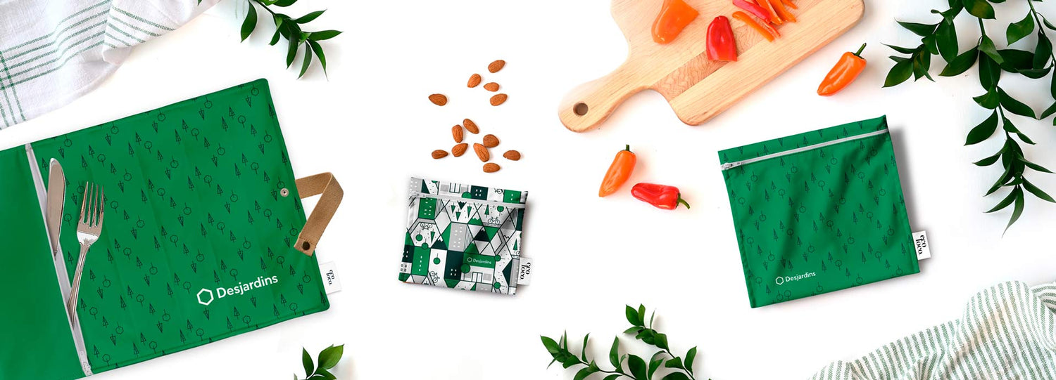 Sacs réutilisables sandwich et collation ainsi qu'un napperon aux couleurs et logo de Desjardins comme objets promotionnels écolo sur fond blanc avec des feuilles, petits poivrons oranges et rouges ainsi que des amandes