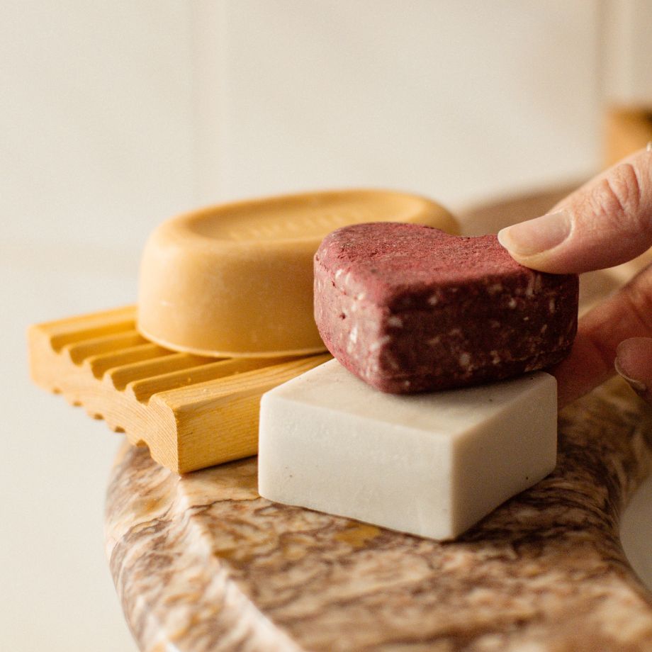 Trois savons fait à la main par Eco Loco sur un comptoir d'une salle de bain avec un porte-savon en bois le mur à l'arrière est blanc