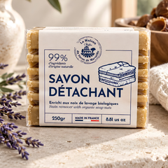 Un savon et son étiquette sur laquelle il est écrit Savon détachant enrichi de noix de lavages biologiques fait en France 250 grammes avec un arrière plan minimaliste. 