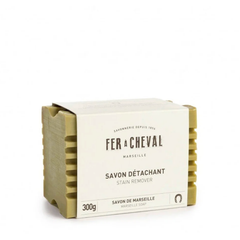Un savon vert avec des stries et une étiquettes ou l'on peut lire:  Fer a cheval, Marseille, Savon détachant, stain remover, savon de marseille 300g sur un fond blanc. 