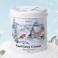 Une boite ronde et blanche avec un dessin de maison et d'un oiseau et des inscriptions Bisou Earl Grey Cream entouré de neige avec un fond bleu. 