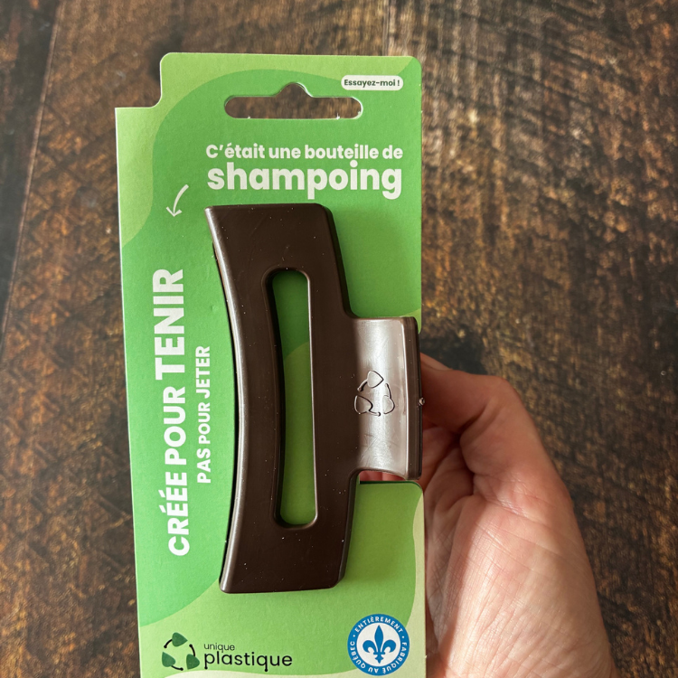 Moyenne pince à cheveux brune avec un logo de matériau recyclé et son emballage cartonné vert qui dit:  C'était une bouteille de shampoing, créée pour tenir pas pour jeter, Unique plastique et le logo fait au Québec. 
