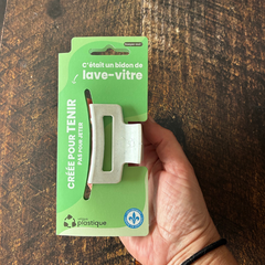 Petite pince à cheveux blanche avec un logo de matériau recyclé et son emballage cartonné vert qui dit:  C'était un bidon de lave-vitre, créée pour tenir pas pour jeter, Unique plastique et le logo fait au Québec. 