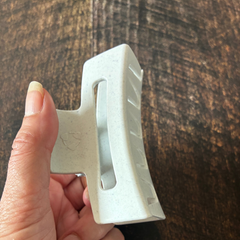 Pince à cheveux blanc avec le logo de matériau recyclé tenu dans une main féminine au dessus d'une planche de bois. 