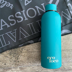 Bouteille d'eau bleue aqua en acier inoxydable sur un fond de bois et une serviette de sport en microfibre