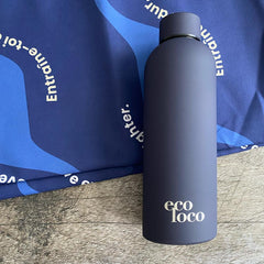 Bouteille d'eau mauve profond violet viollette en acier inoxydable sur un fond de bois et une serviette de sport en microfibre